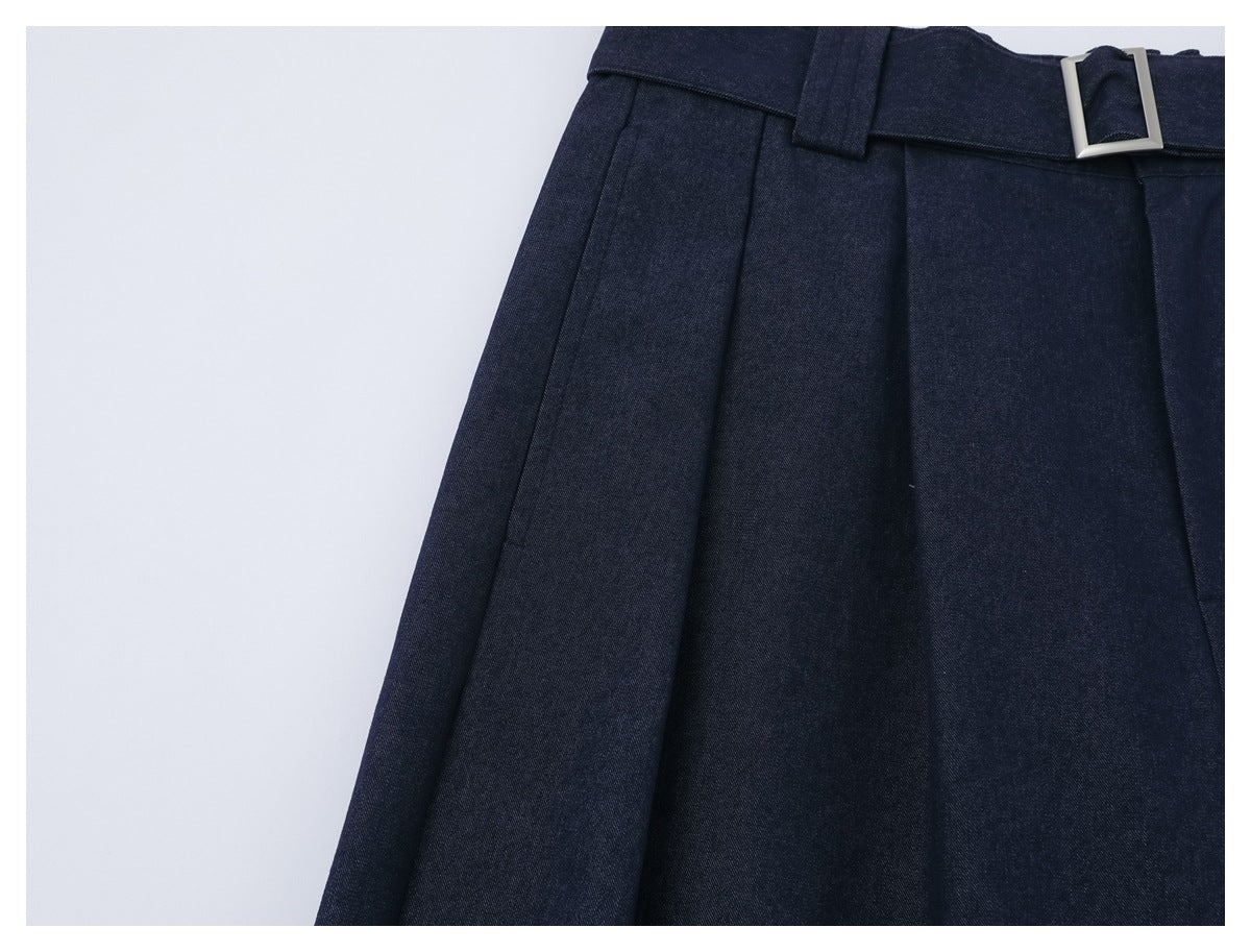 Close-up of dark navy trousers showing the waistband, belt loops, pleats and rectangular silver buckle.