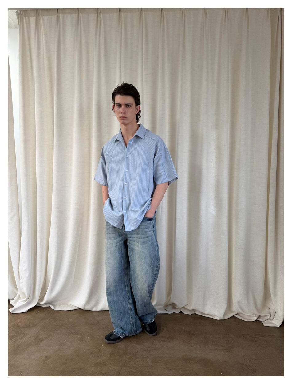 Model wearing a light blue striped short-sleeve button-up shirt with loose, faded blue jeans.