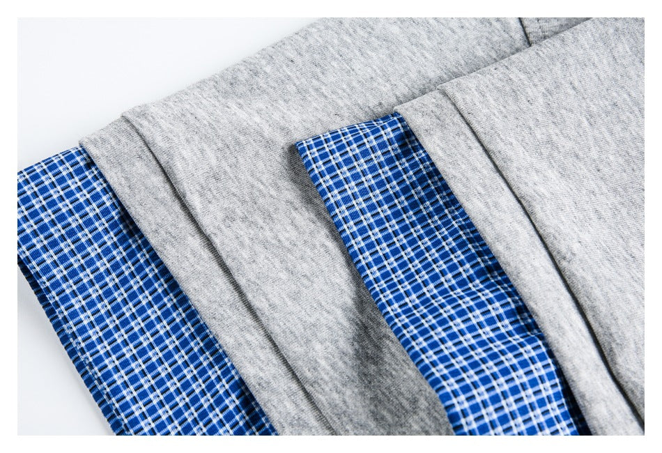 Close-up of heather gray fabric with blue-and-white plaid sections and folded seams.