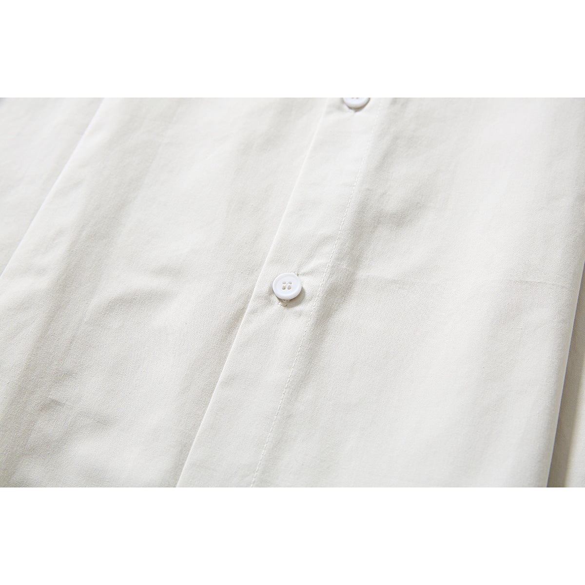 Close-up of an ivory shirt's button placket, white buttons, and plain fabric.
