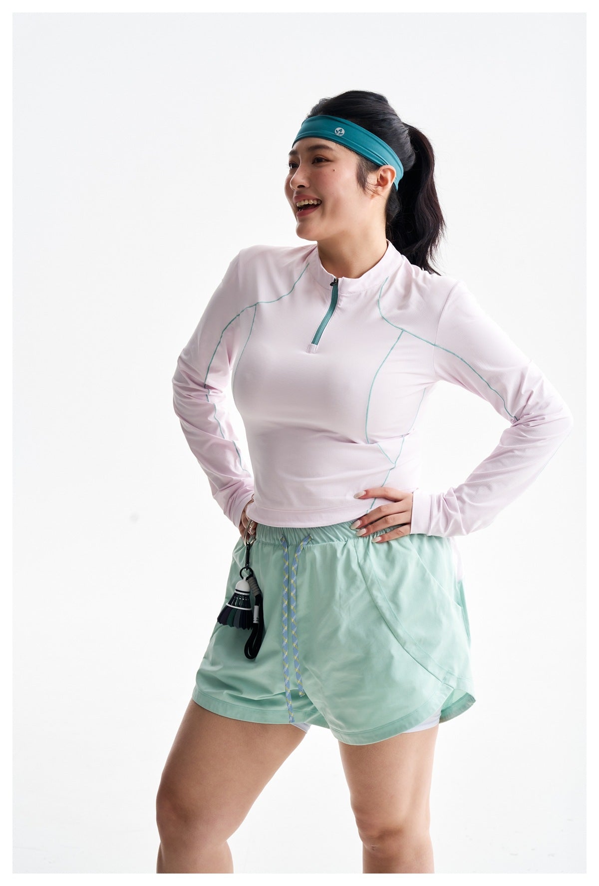 Model wearing a pale pink long-sleeve quarter-zip top with teal seam accents and mint running shorts.