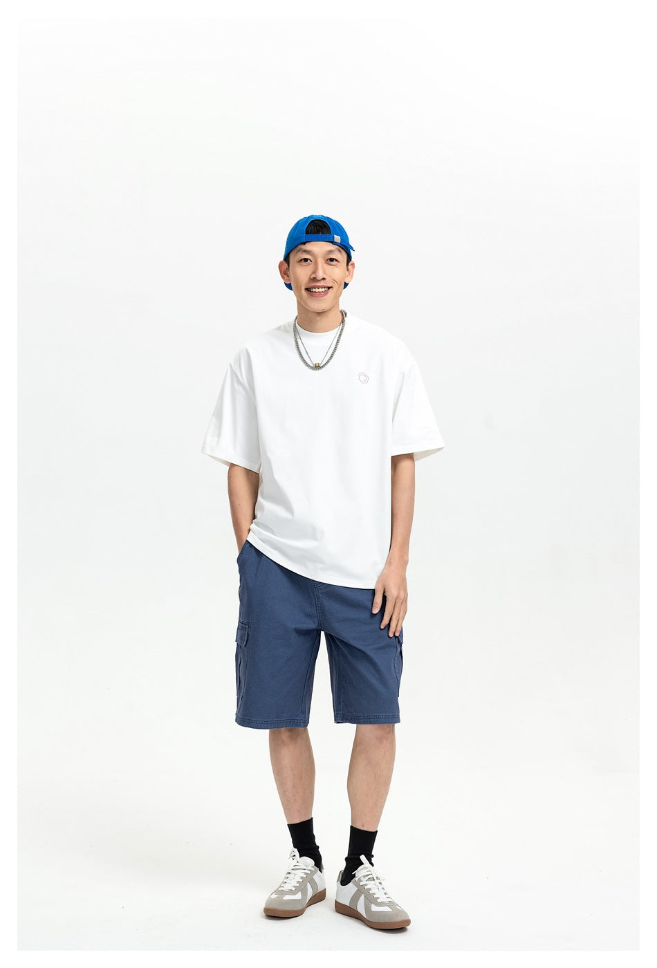 Full-length front view of a man in a white oversized T-shirt with a tiny chest emblem and blue cargo shorts.