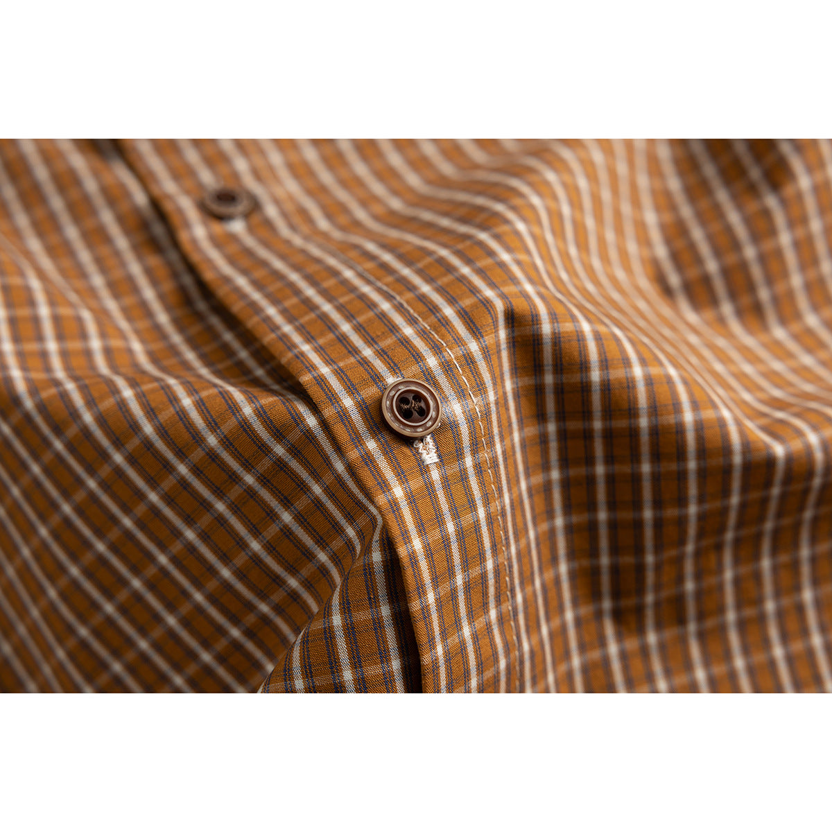 Close-up of a brown and orange plaid shirt placket with a dark button and white stitching.