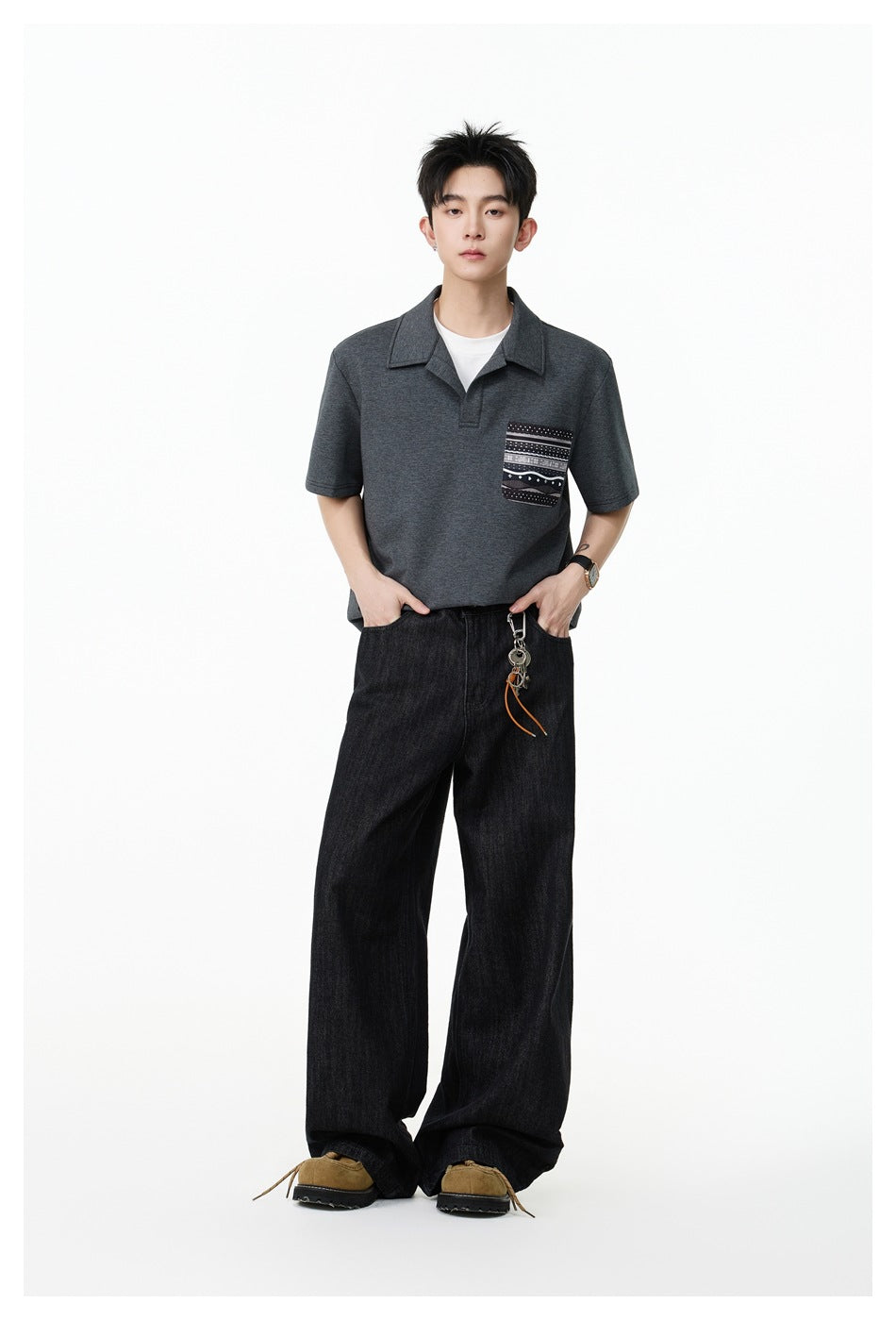 Full-length front view of a model wearing a charcoal polo with a patterned chest pocket and wide black jeans.