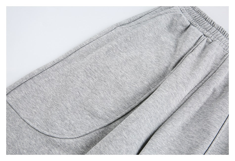 Close-up of light gray heather sweatpants showing a curved patch pocket and waistband.