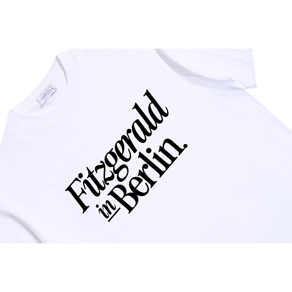 Angled close-up of a white T-shirt with black “Fitzgerald in Berlin” lettering across the chest.