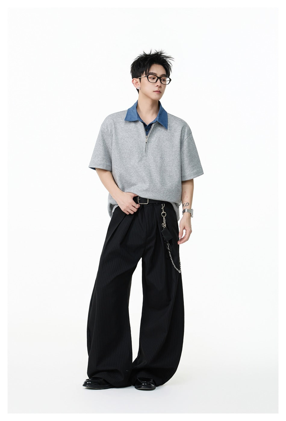 Model wearing a gray short-sleeve top with a blue collar and quarter zip, styled with black pinstripe wide-leg trousers.