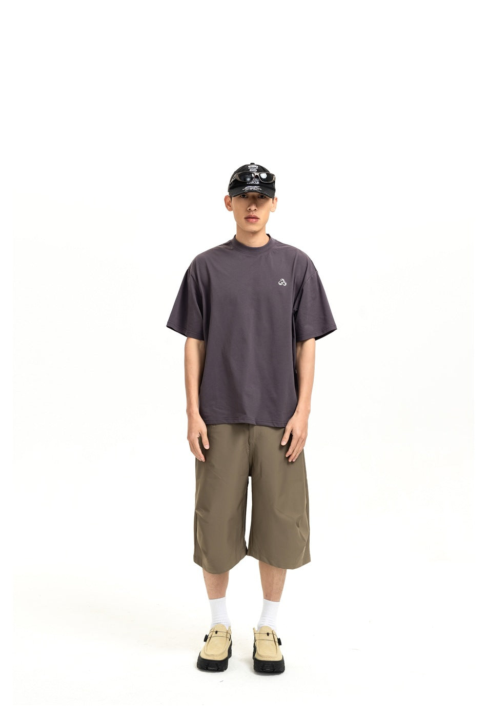 Full-length front view of a model wearing a charcoal oversized T-shirt with a small chest emblem and olive knee-length