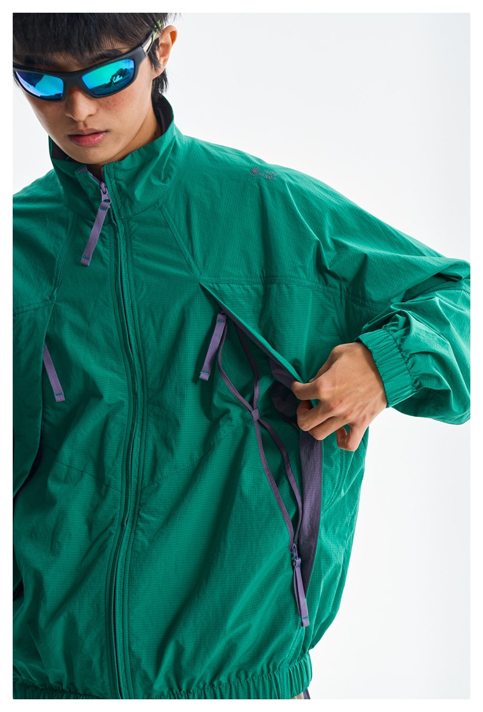 Close-up of a model opening the teal jacket's underarm ventilation panel, showing purple zippers and straps.