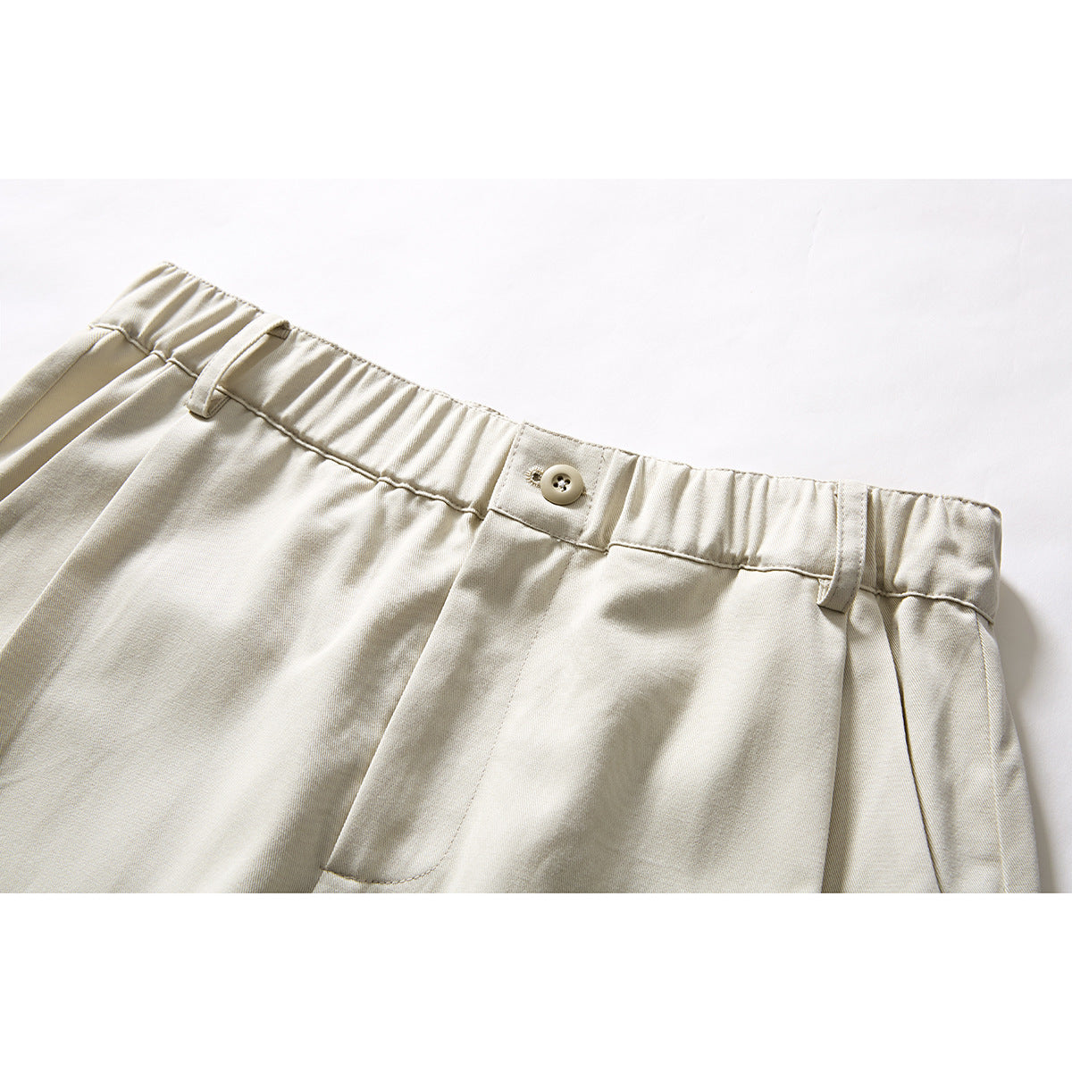 Close-up of cream shorts showing the elasticated waistband, button, belt loops and front pocket edge.