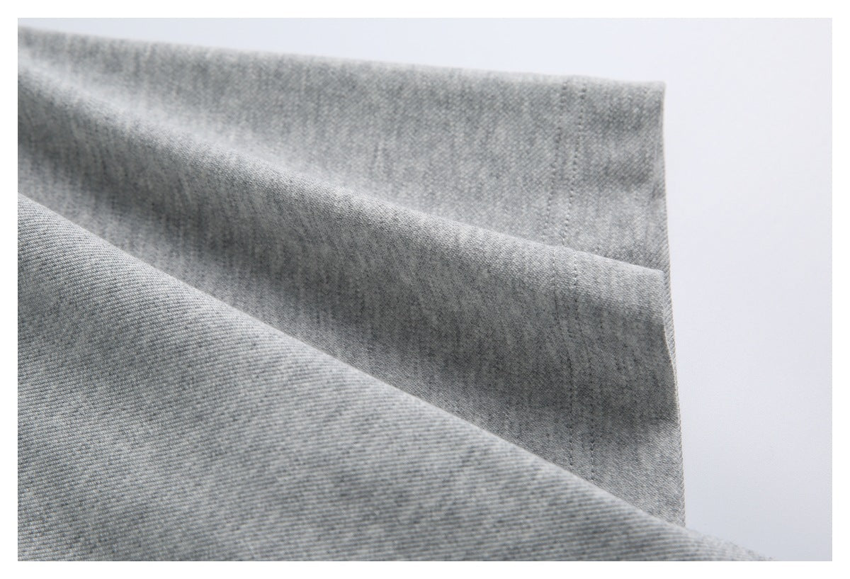 Close-up of gray garment fabric draped into folds, showing a stitched edge.