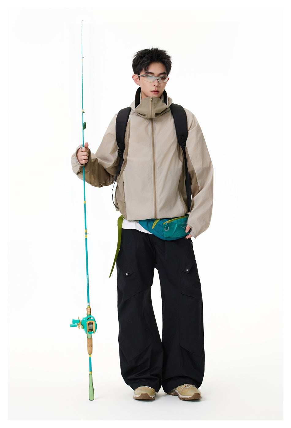 Full-length model wearing a light beige hooded zip jacket with black cargo pants and a teal waist bag.