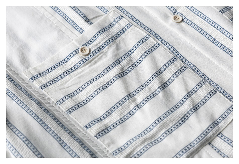Close-up of a buttoned chest pocket on a white shirt with narrow blue patterned stripes.
