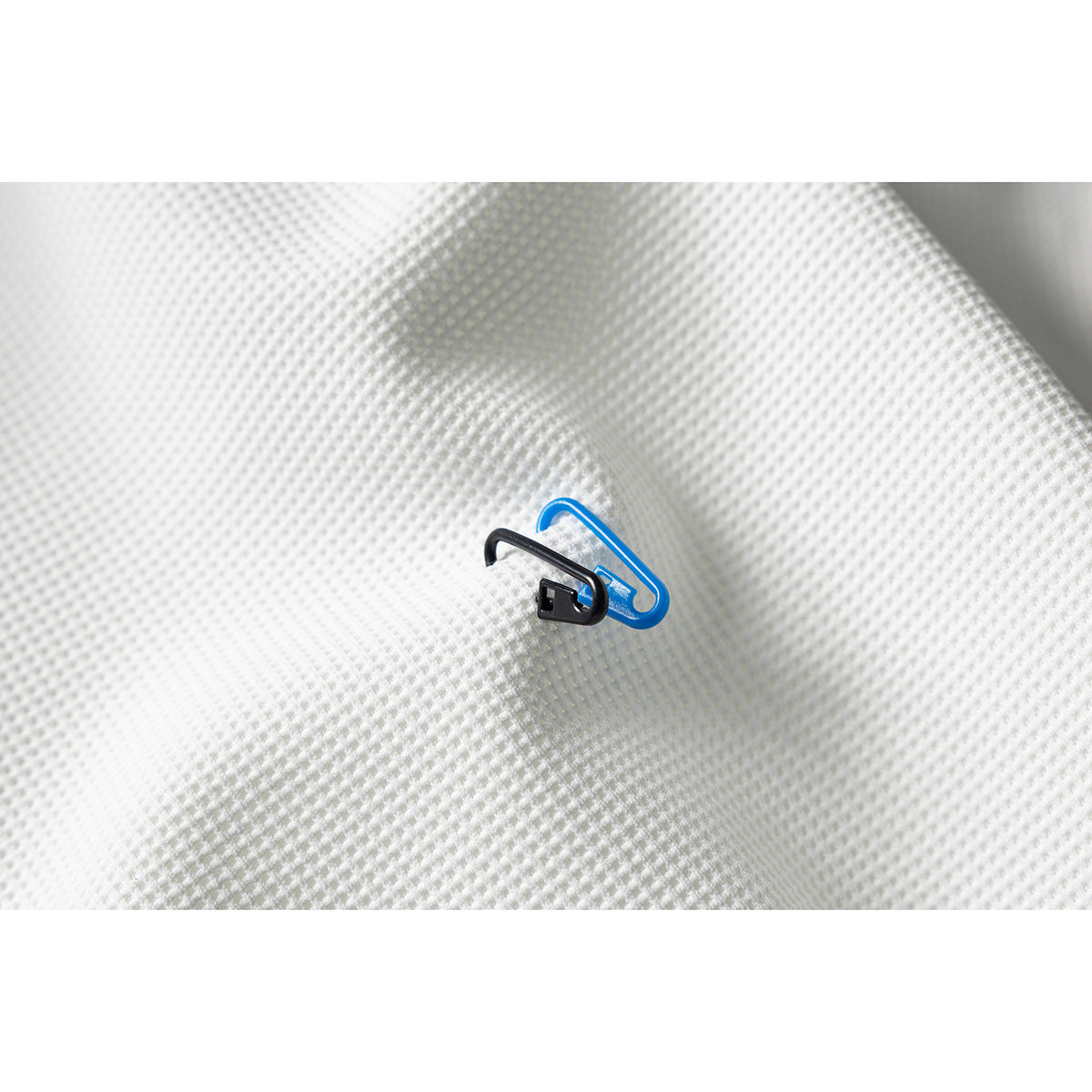 Close-up of white textured fabric with small black and blue plastic pieces resting on it.