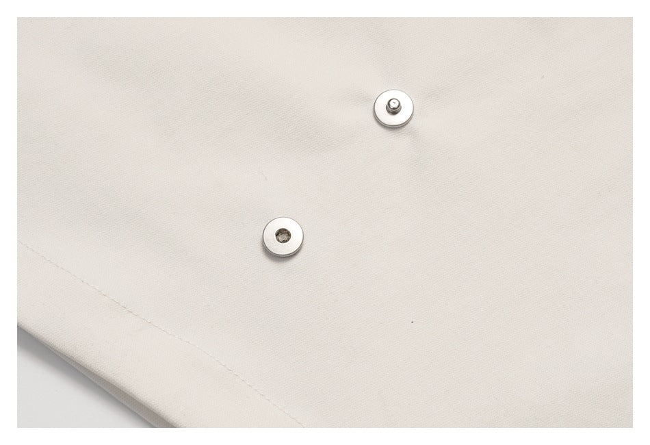 Close-up of two round metal snap fasteners on cream fabric.