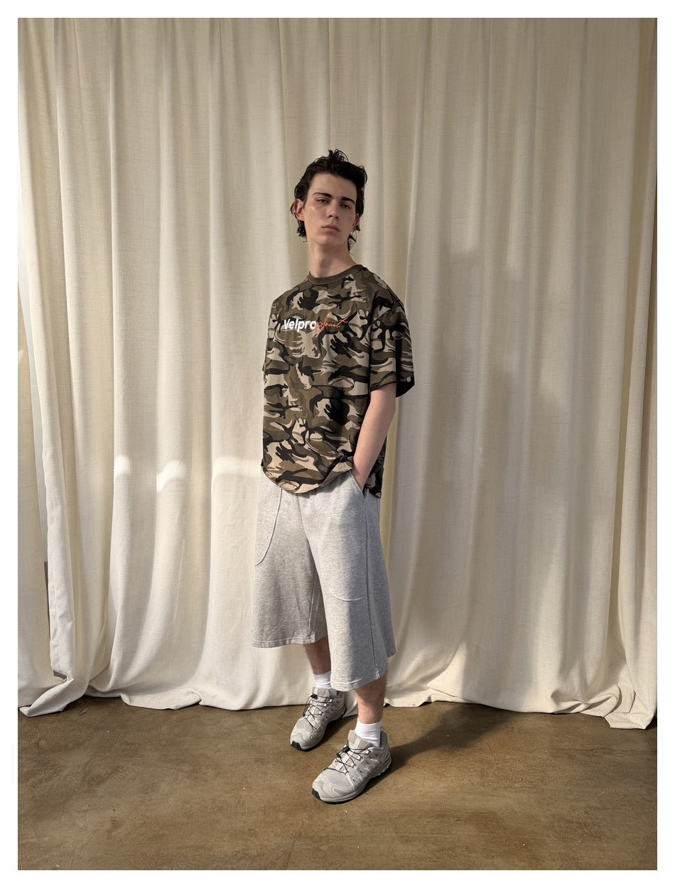 Model wearing a gray-brown camouflage graphic T-shirt with light gray long shorts.