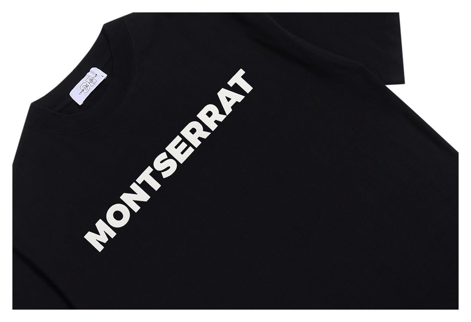 Close-up of a black T-shirt front with bold white diagonal “MONTSERRAT” lettering.