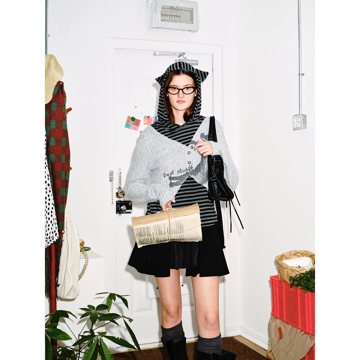 Model wearing a black-and-gray striped hooded top under a cropped light-gray buttoned cardigan and black skirt.