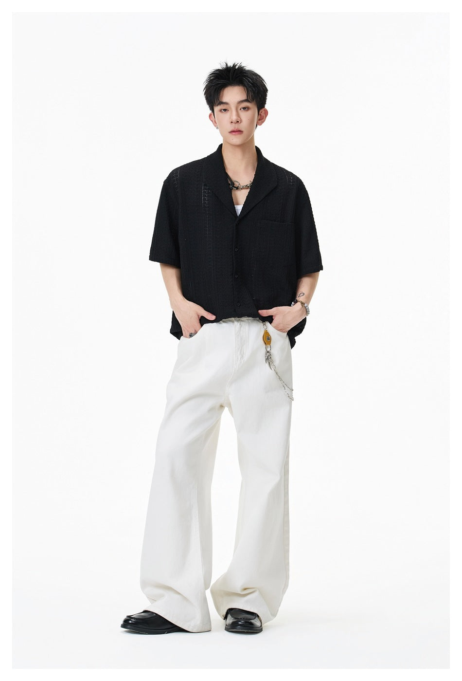 Full-length model wearing a black short-sleeve textured button-up shirt with wide white trousers.