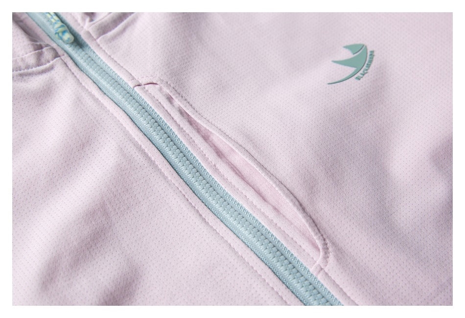 Close-up of a small green chest emblem, front zipper, and pocket seam on the pale pink jacket.