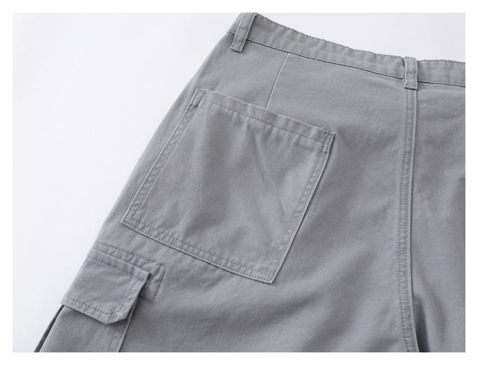 Close-up of gray trousers showing a large rear patch pocket, a smaller flap pocket, belt loops, and stitching.