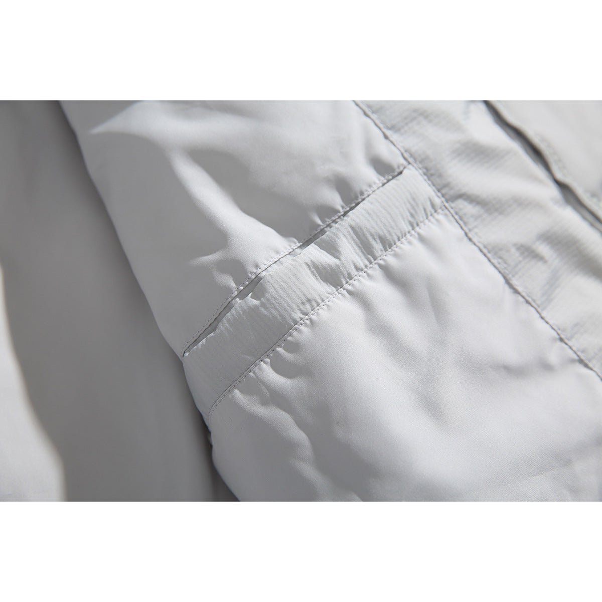 Close-up of a pale gray jacket showing a stitched seam across smooth and subtly textured fabric panels.