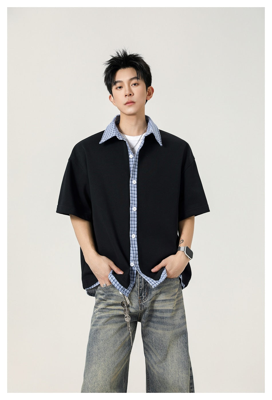 Model wearing an oversized black short-sleeve shirt with a blue plaid collar, button placket and hem trim.