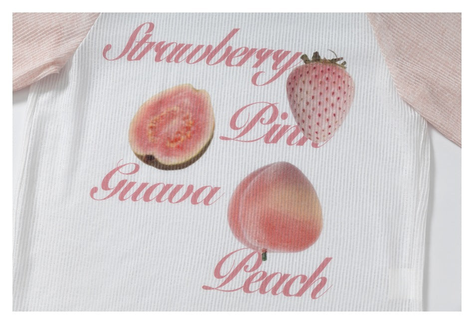 Close-up of a white ribbed garment with pink sleeves and pink fruit illustrations and script reading Strawberry, Guava, and