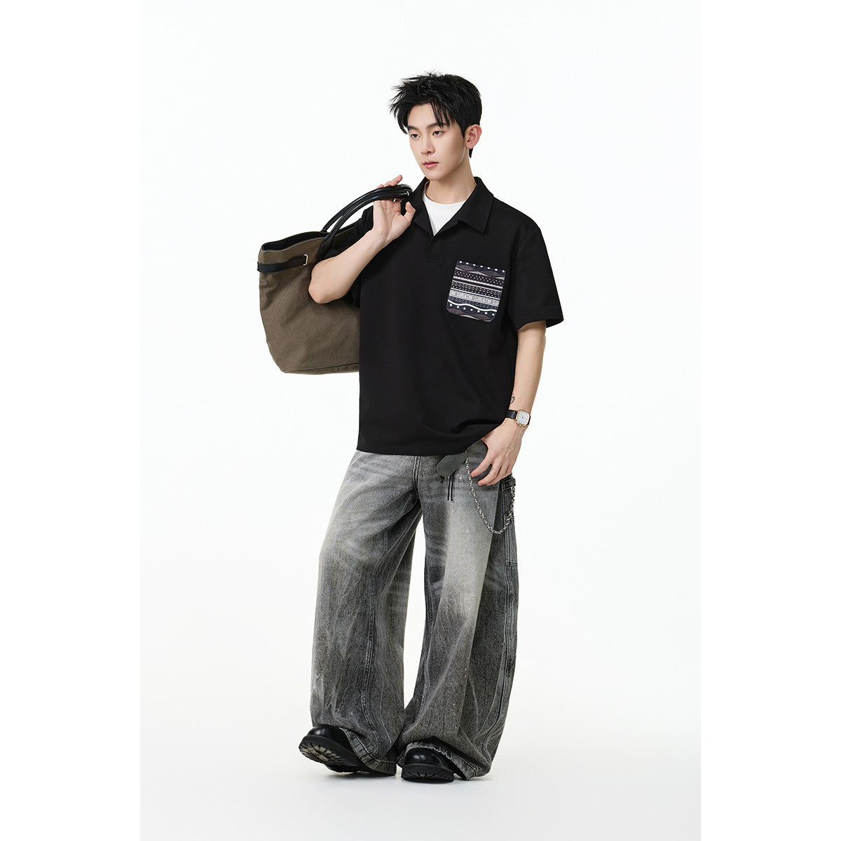 Model wearing a black short-sleeve collared polo with a patterned chest pocket and wide gray jeans.