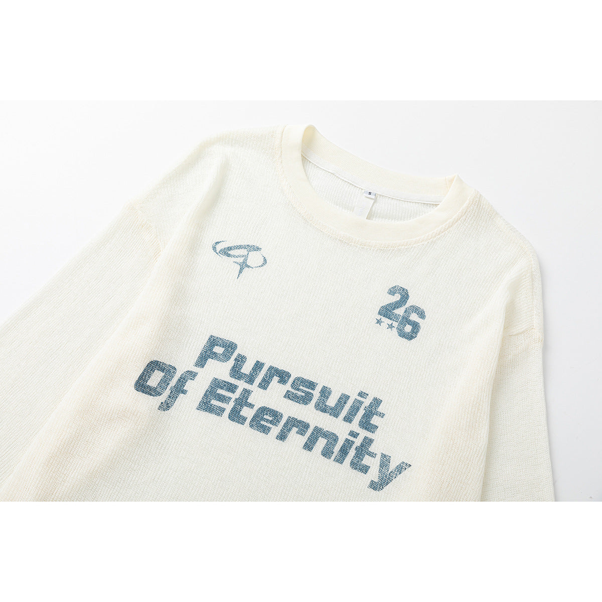 Close-up of an ivory knit long-sleeve shirt with blue “Pursuit of Eternity” chest print and a small 26 graphic.