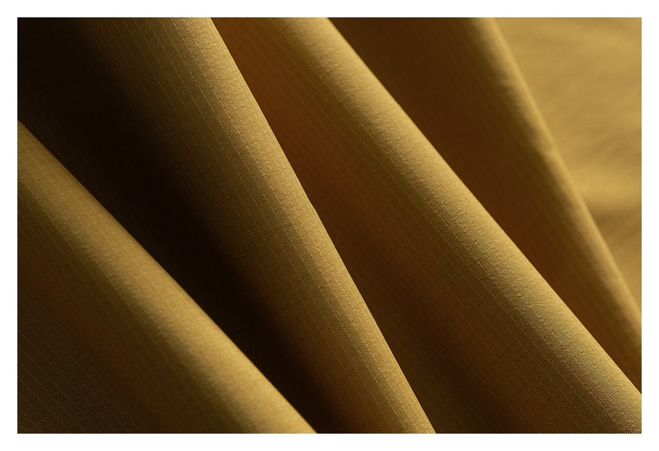 Macro view of the fine texture and folds of mustard-gold trouser fabric.