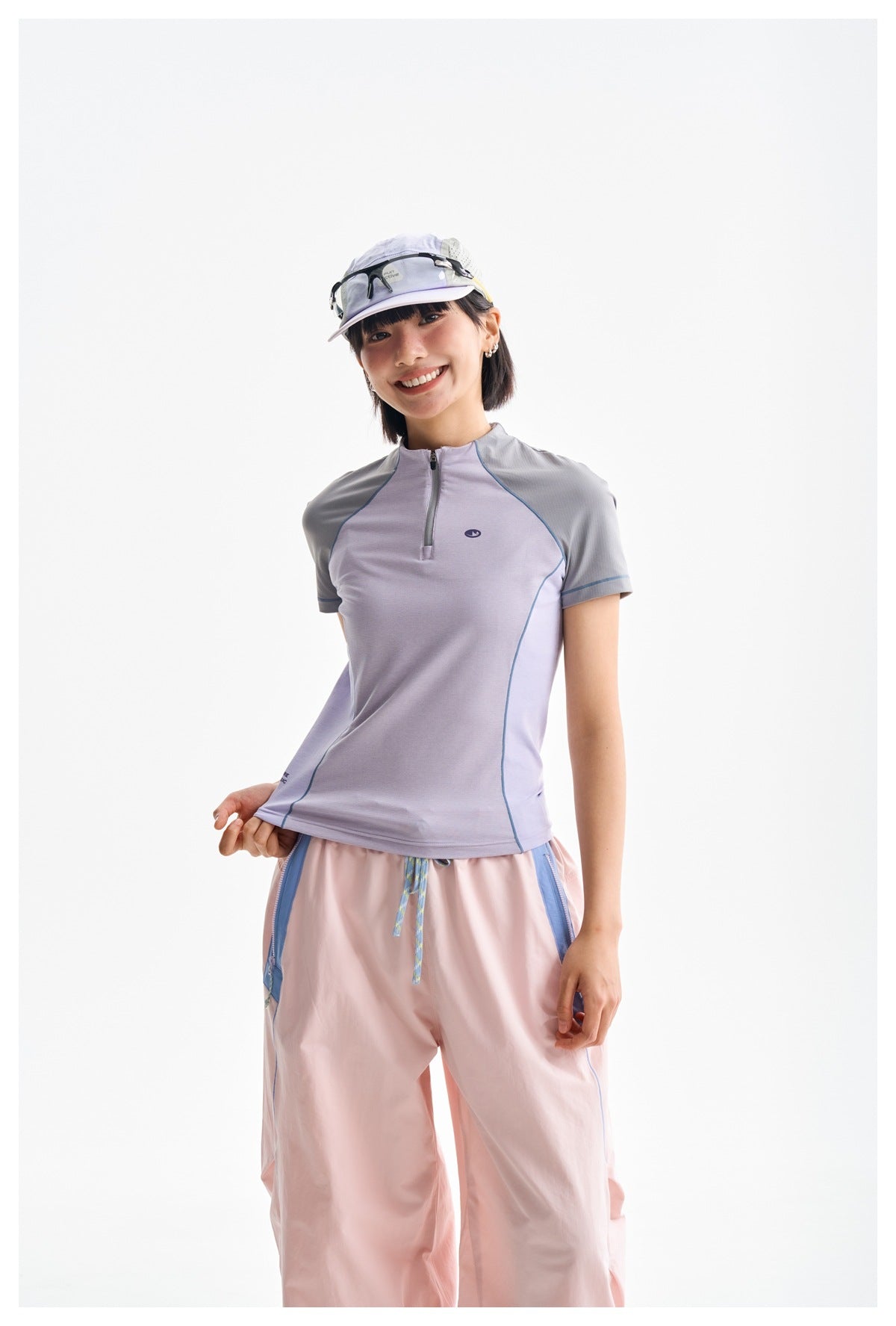 Model wearing a lavender and gray zip-neck top with pink trousers, shown from the front.