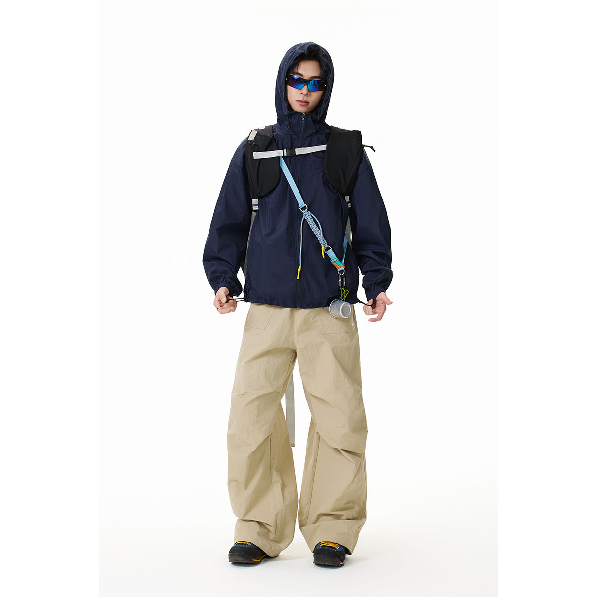 Model in a navy hooded jacket and beige wide-leg pants, wearing a backpack and sunglasses.
