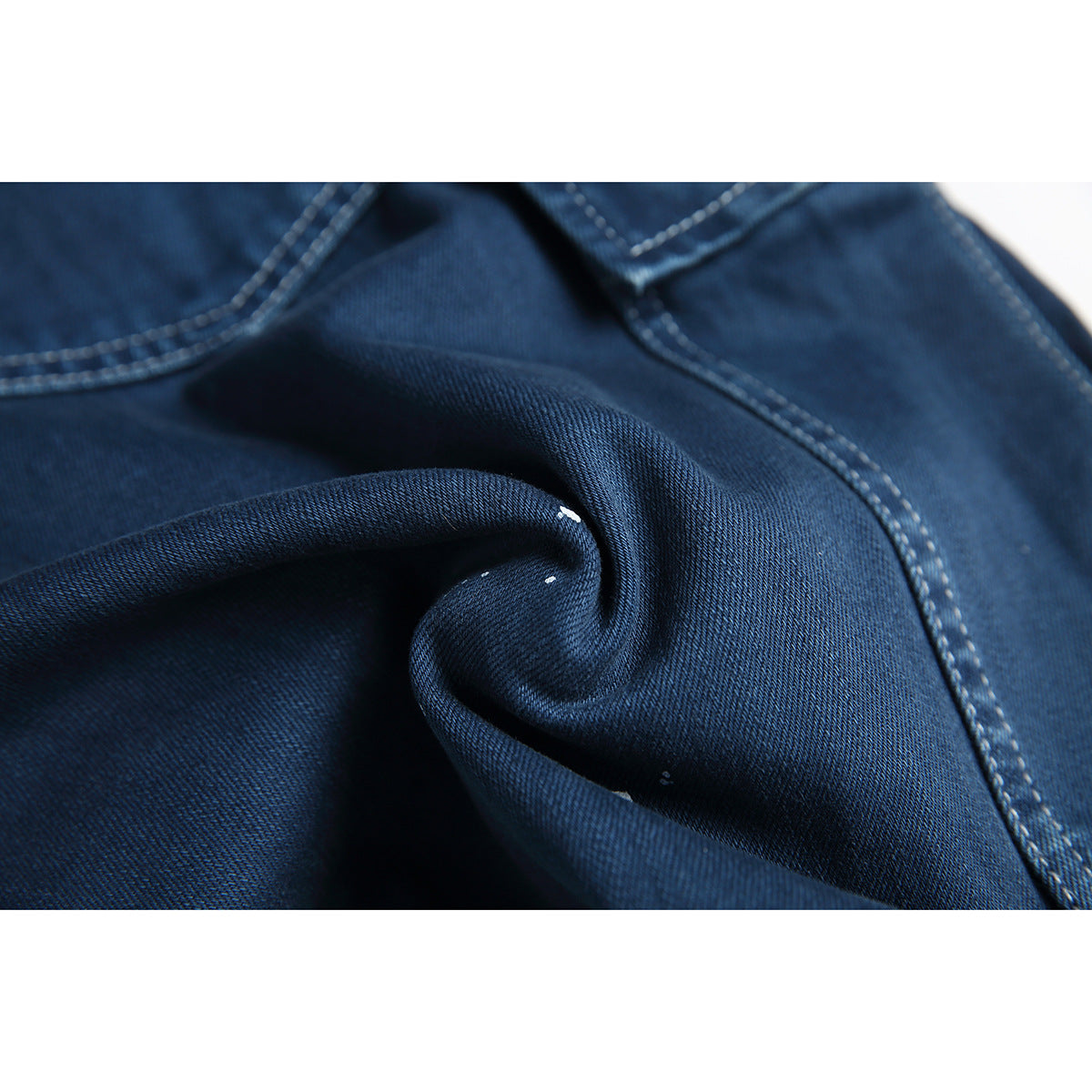 Macro detail of dark blue denim fabric folded to show its weave, pale stitching, and small white specks.