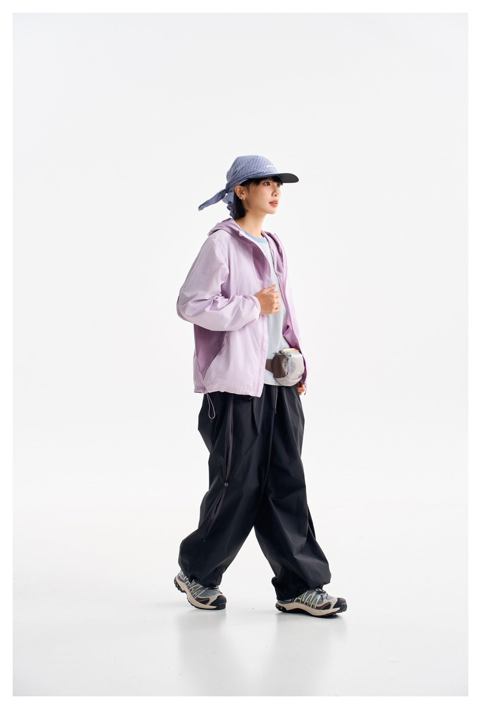 Model wearing a lilac hooded zip jacket and loose black pants, shown full length in a blue plaid cap.