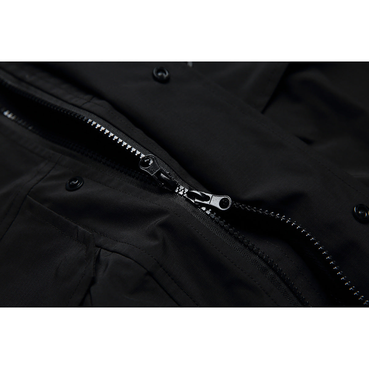 Close-up of a black jacket's two-way zipper and snap fasteners.