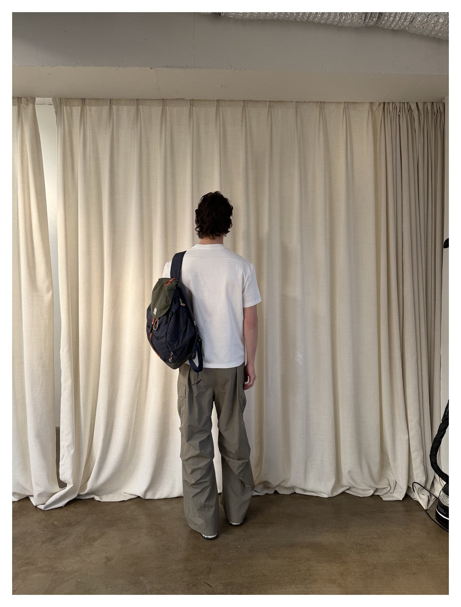 Full-length rear view of a model wearing a plain white T-shirt and loose gray cargo pants, with a backpack.