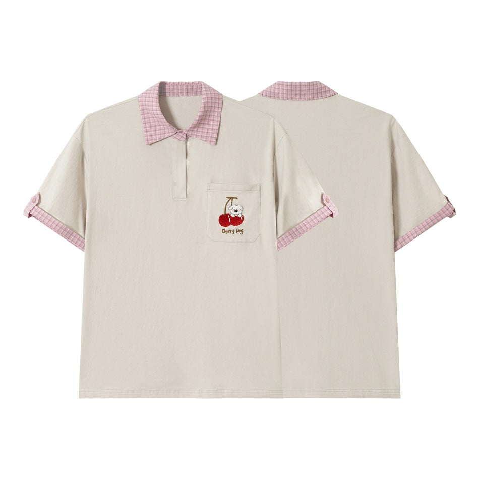 Cream short-sleeve polo shown from front and back, with a pink plaid collar and cuffs and dog-and-cherry pocket embroidery.