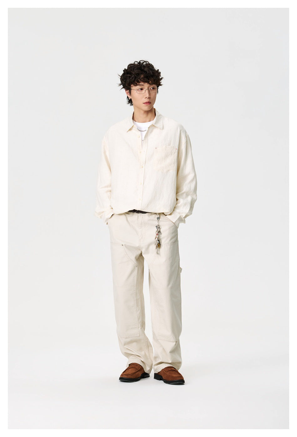 Full-length model wearing an ivory button-up shirt, light utility trousers, and brown loafers.