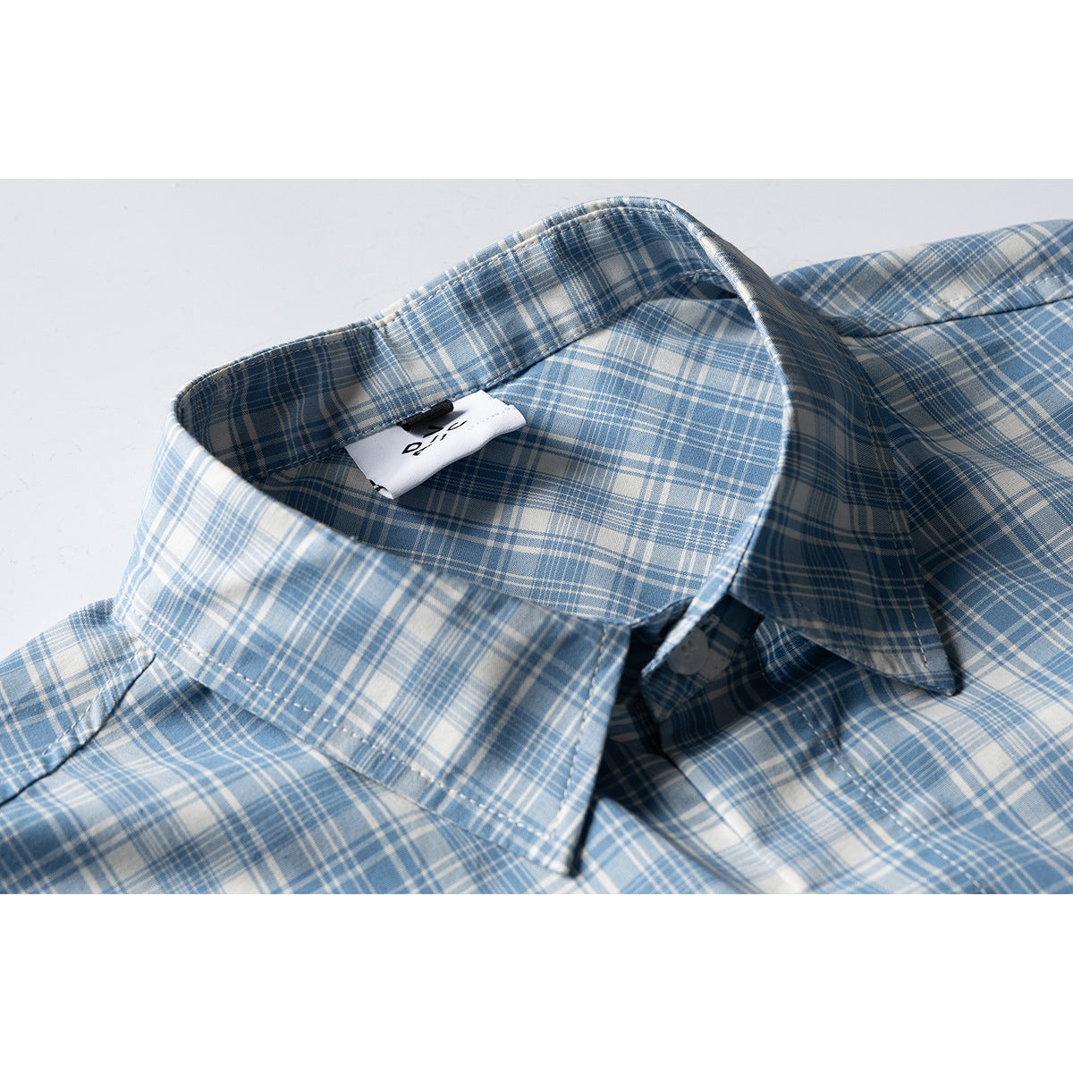 Close-up of a blue-and-white plaid short-sleeve shirt collar, placket, and sewn-in label.
