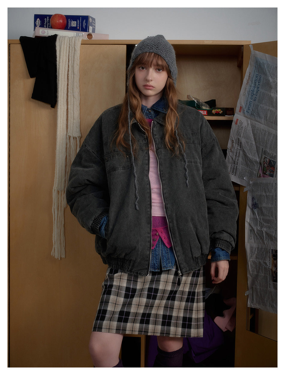 Front view of a model in an oversized charcoal jacket with a front zipper, elastic cuffs and hem, and a plaid skirt.