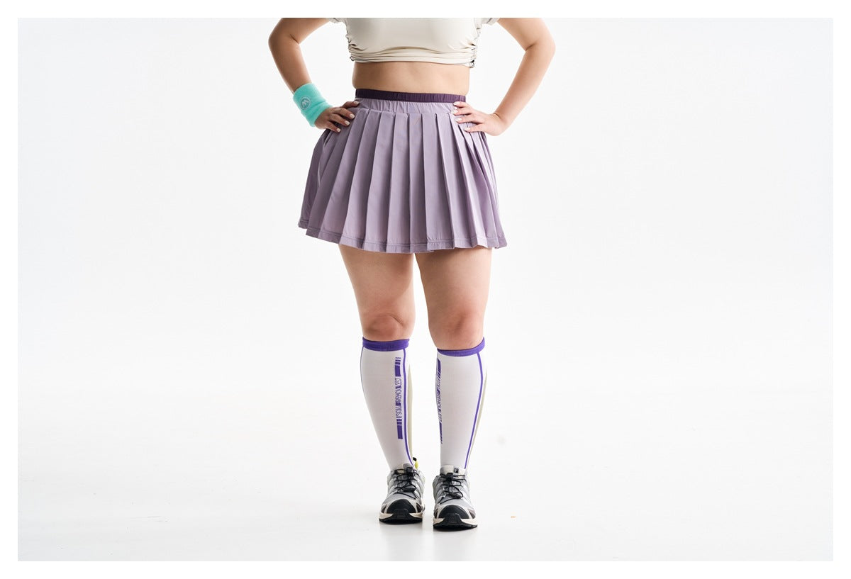 Front view of a model in a pleated lavender athletic skirt with a dark waistband and knee-high socks.