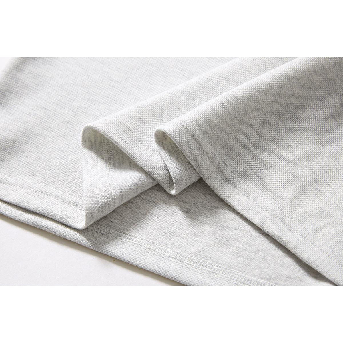 Close-up of folded light gray polo fabric showing the sleeve edge and stitched hem.