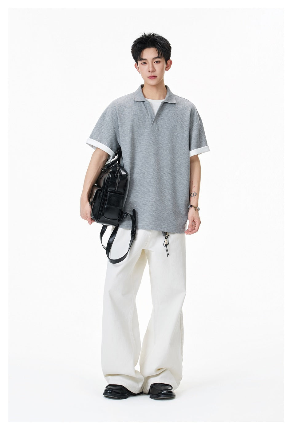 Standing model wearing an oversized light gray collared shirt with white cuffs and loose white trousers.