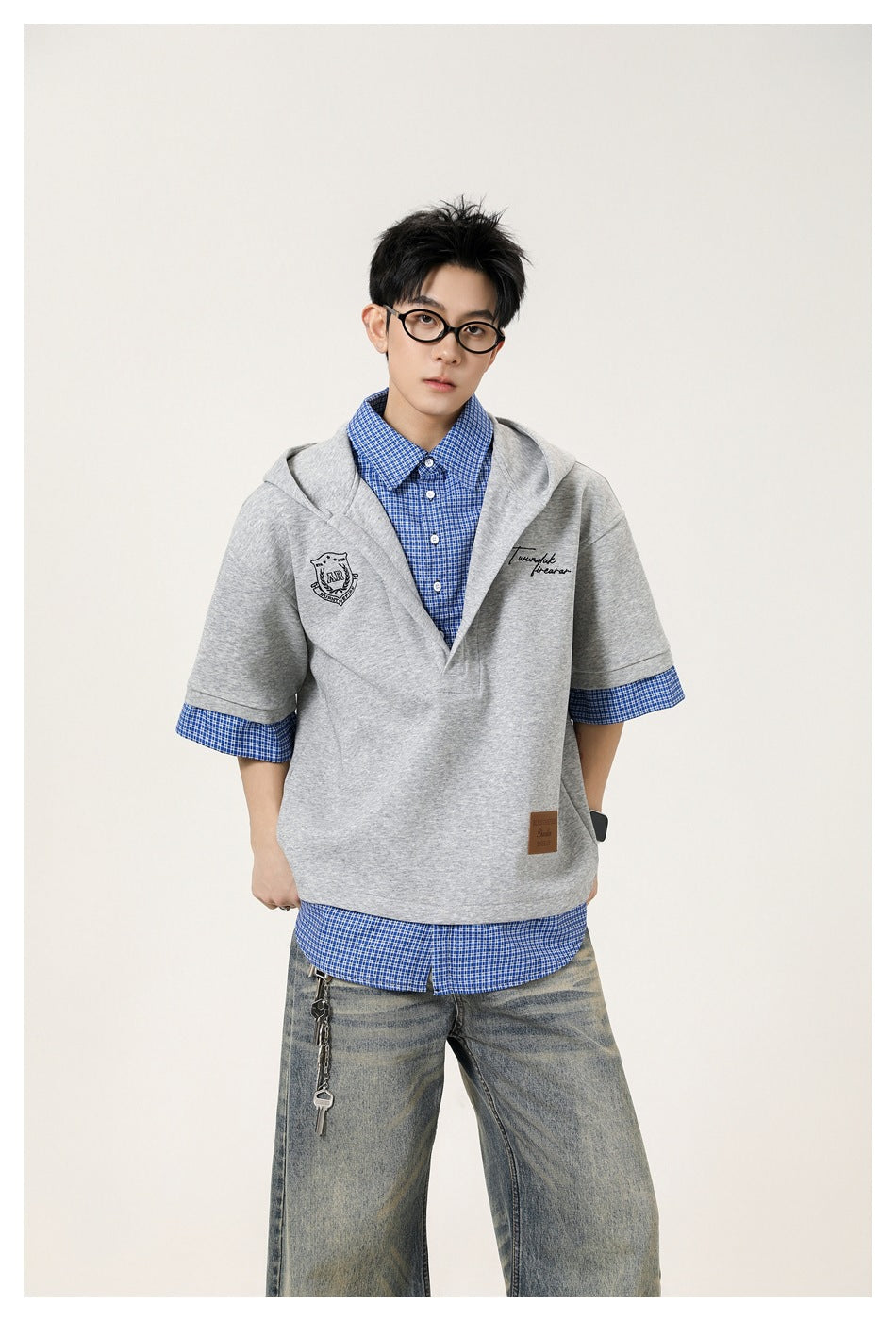 Front view of a model in a light gray short-sleeve hooded pullover layered over a blue checked shirt.