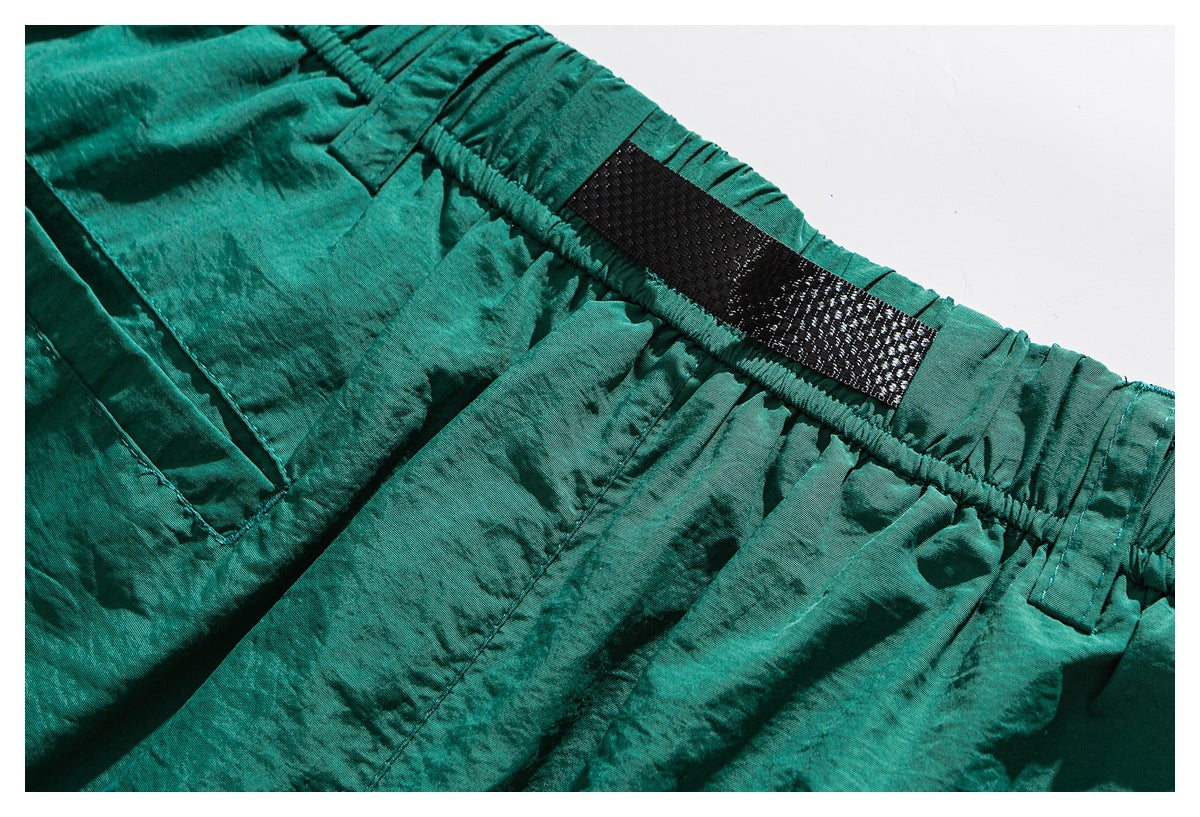 Close-up of teal shorts with an elastic waistband, black webbing detail and a stitched pocket.