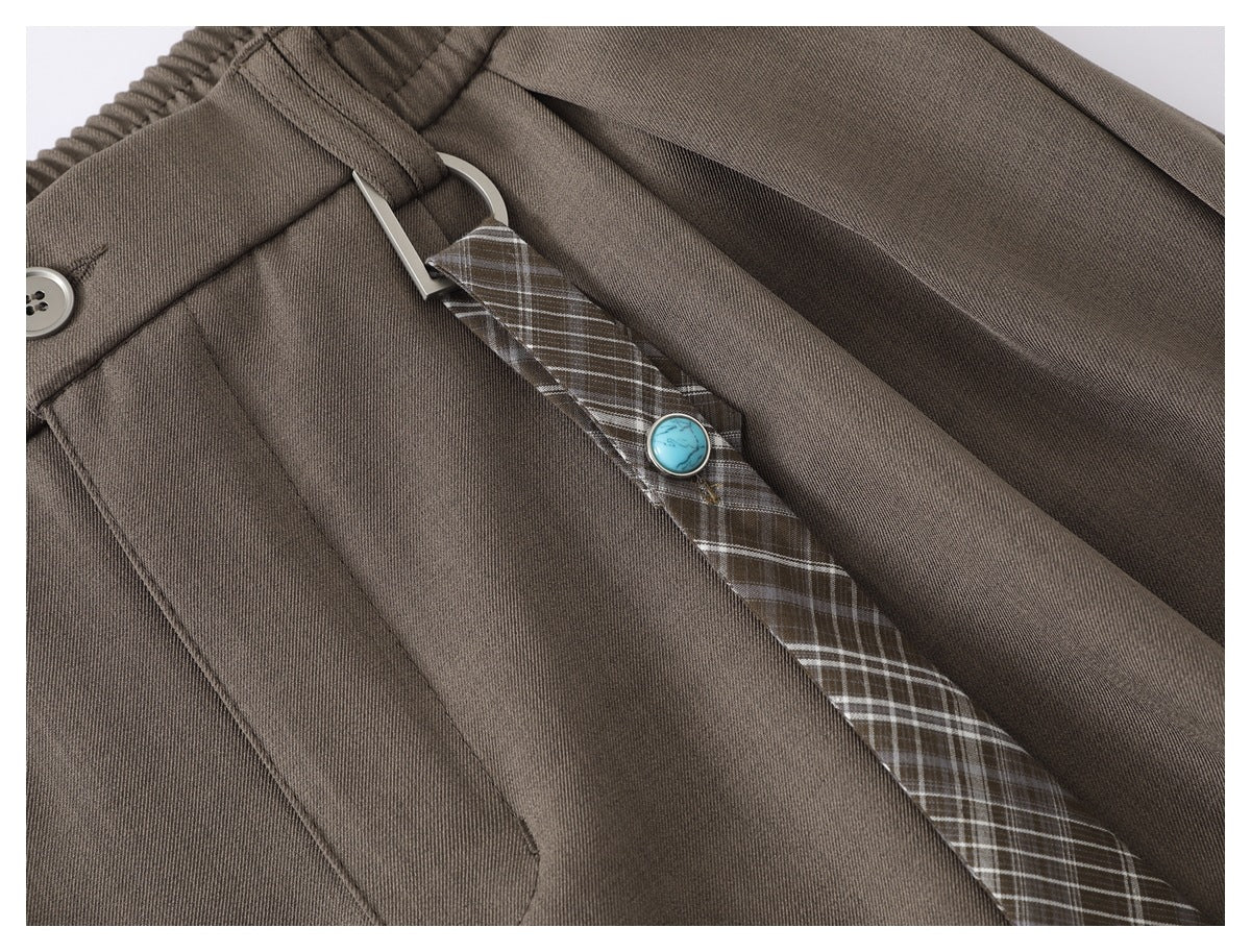 Close-up of taupe trousers showing a plaid belt accent, silver buckle, and turquoise button.