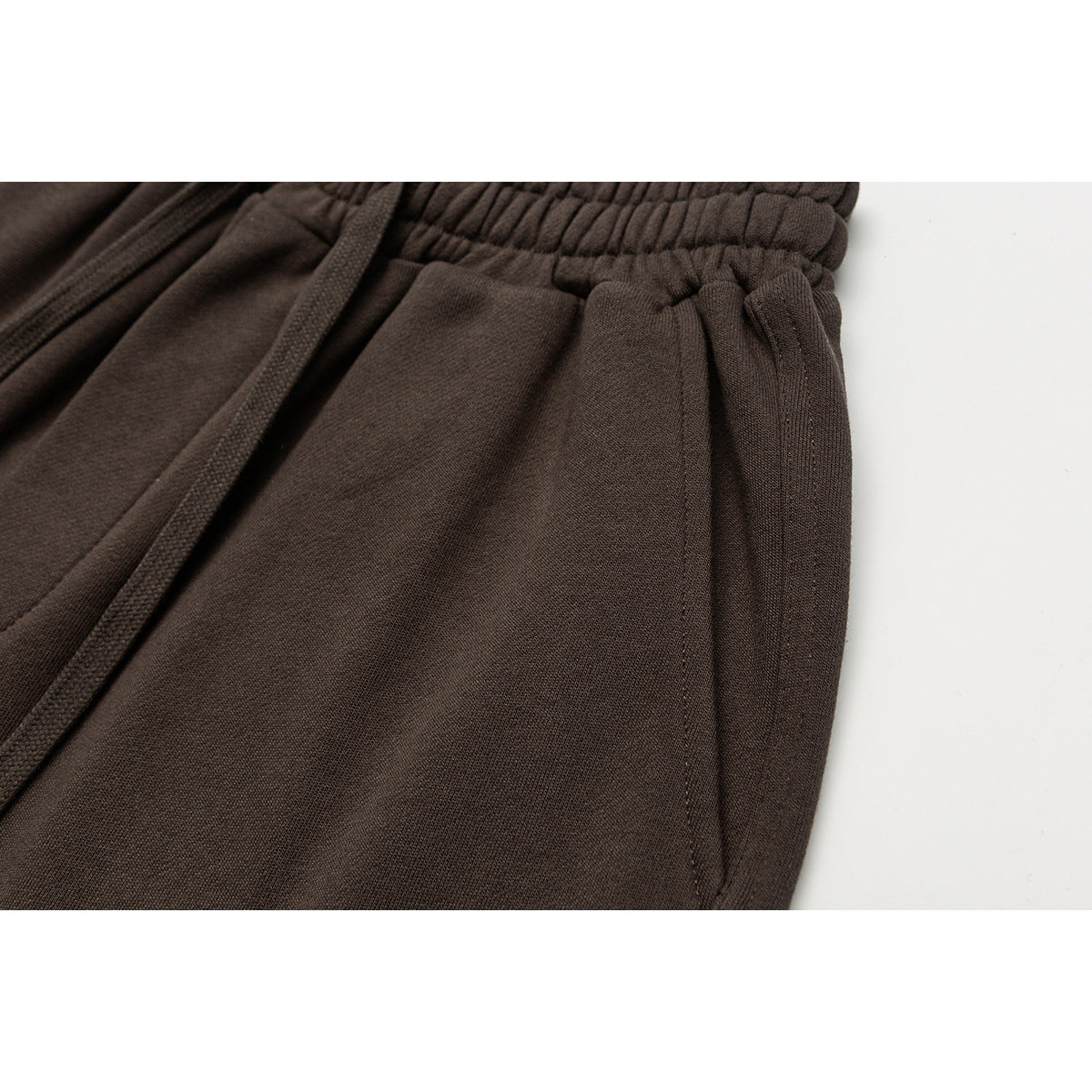 Close-up of brown shorts showing the elastic waistband, drawstring, and side pocket.