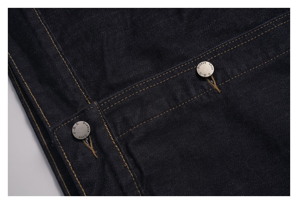 Close-up of two metal buttons and contrast stitching on dark indigo jacket fabric.