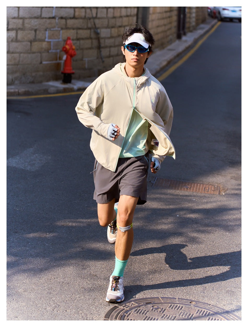 Model running outdoors in a light beige jacket with pale aqua zipper trim and dark shorts.